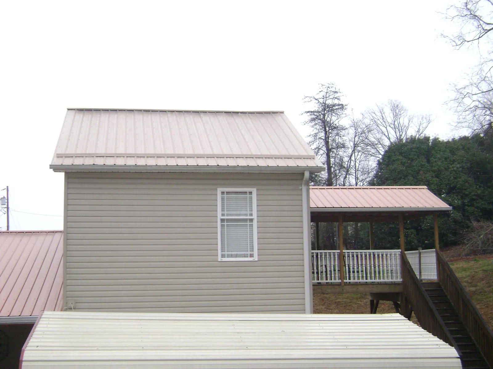 Tan metal roofs on a two story addition and attached porch, from a Roof Replacement job in Waterville